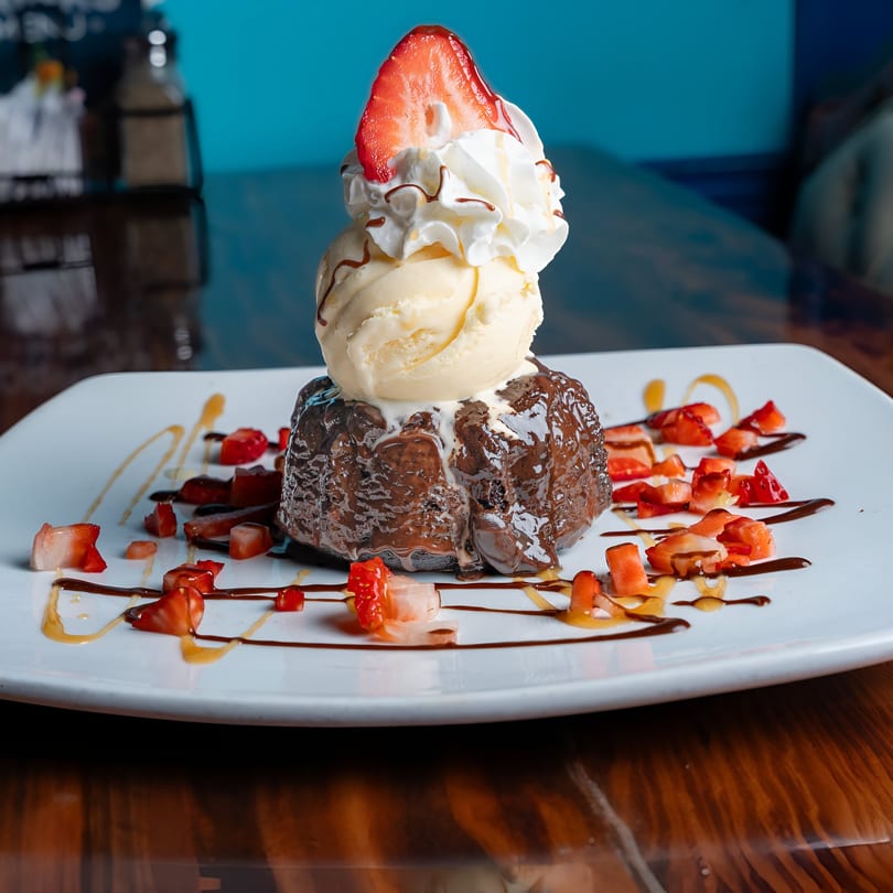 Chocolate lava cake with vanilla ice cream, whipped cream, strawberry, and chocolate drizzle.