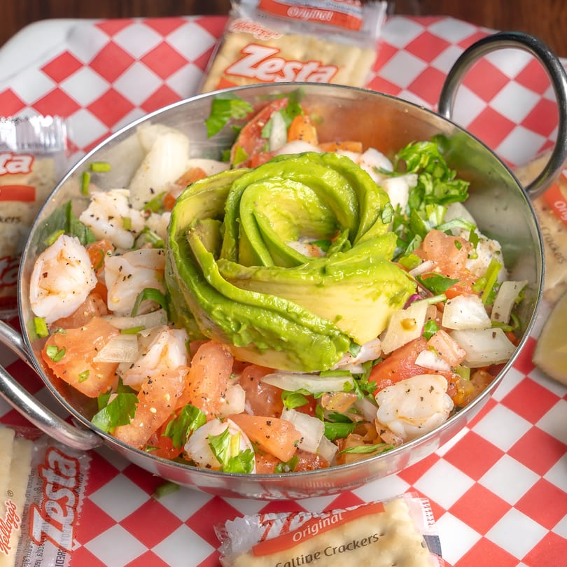Shrimp ceviche with avocado, tomatoes, onions, and cilantro in a metal bowl with crackers.